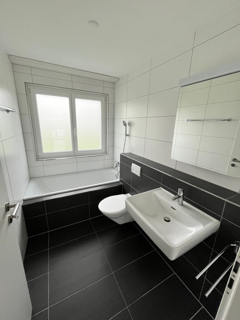 Bathroom with white and black tiles, bathtub, toilet, sink, mirror, and shower head