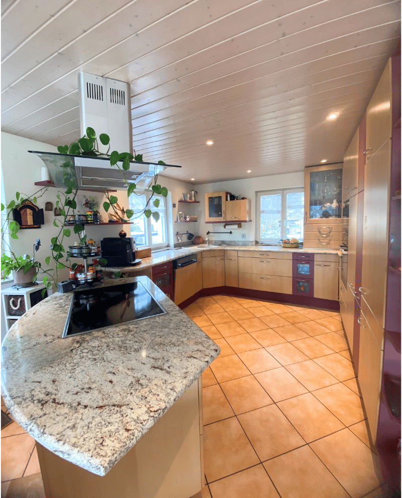 large kitchen with granite countertop, induction hob, kitchen island, wooden cabinets, tile flooring, hanging plants, overhead cabinets