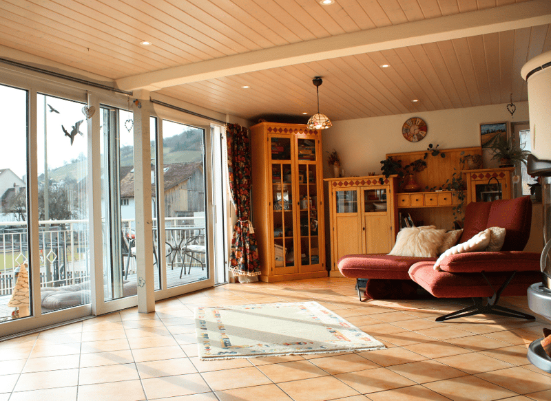 wooden cabinet, couch, chair, carpet, lamps, table, plants, glass door leading to balcony, balcony with chairs and table, mountain view