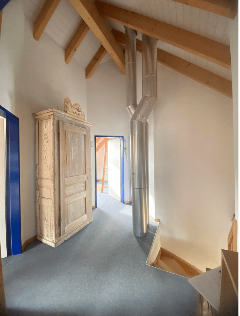 Room with wooden wardrobe and wooden beams ceiling, a ladder leads to the top floor.