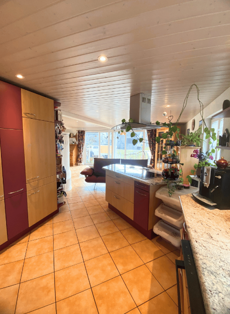 Open kitchen with wooden cabinets, tiled floor, granite countertop, gas stove, extractor fan, various appliances, chairs, couch, table, and window