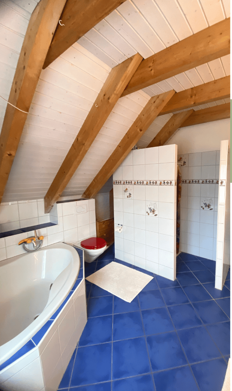 Attic bathroom with wooden beams, blue tiles, bathtub, shower, toilet, white towels