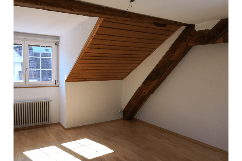 Empty attic room, slanted ceiling, wooden floor, white walls, large window