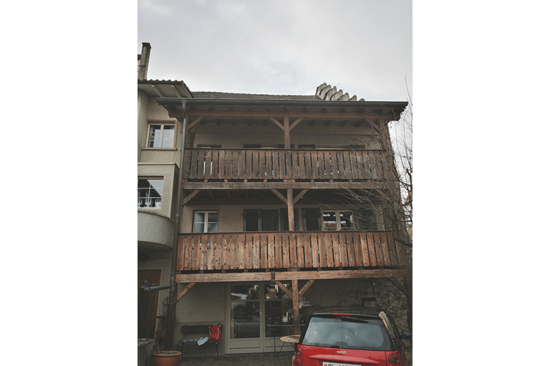 2 story house, wooden balcony, grey roof, brick walls