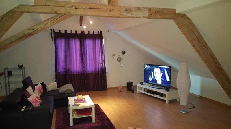 Attic living room with exposed wooden beams, purple curtains, TV stand, coffee table, and a fireplace