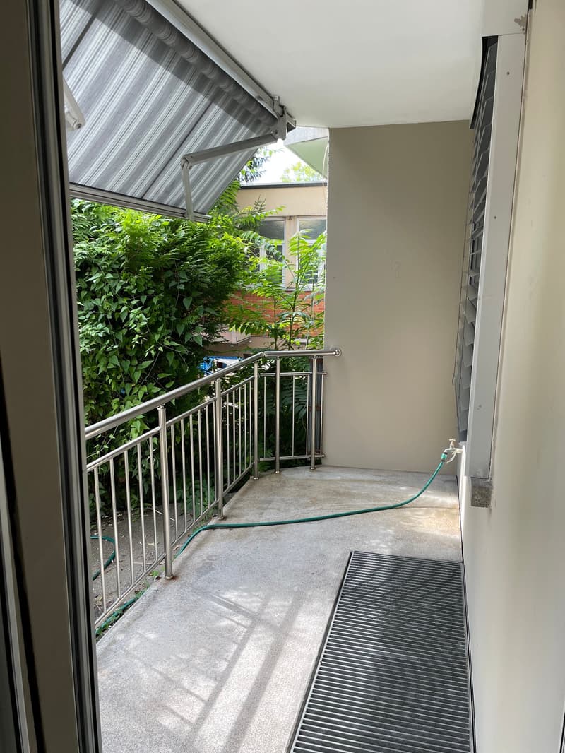 Balcony with metal railings, concrete floor, awning, green hose, plants