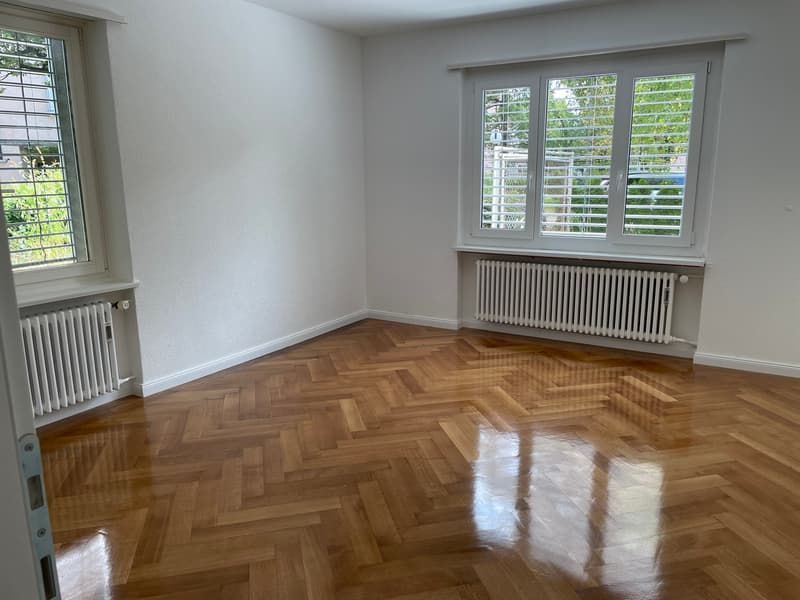 empty room, wooden parquet floor, white walls, two windows with shutters, radiators