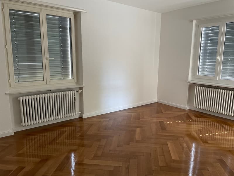 empty room, wooden parquet floor, white walls, two windows with shutters, white radiators