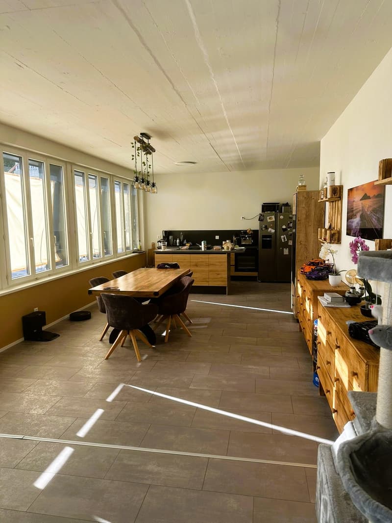 Open plan kitchen and dining area, wooden dining table, wooden chairs, wooden cabinets, large windows, tiled floor, modern appliances