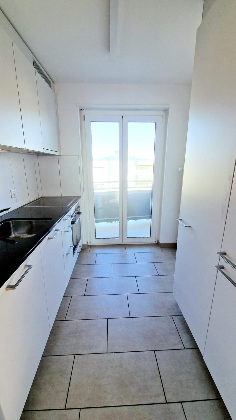 Open plan kitchen with dining area, large windows with doors to terrace, granite countertops, modern appliances, tiled floor.