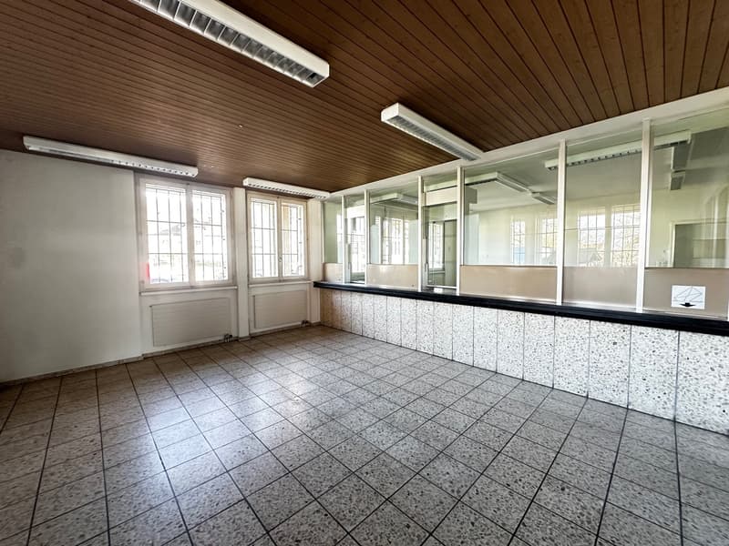 large empty room with large windows, tiled floor, wooden ceiling, fluorescent lights, radiators