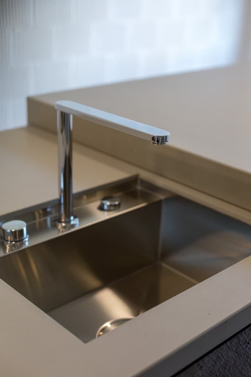 Stainless steel sink, modern faucet, white countertop, silver drain