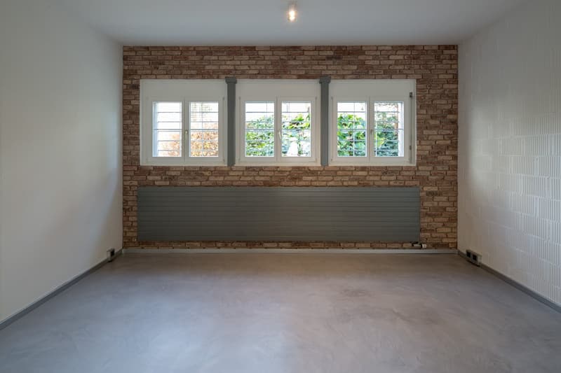 Empty room with brick wall, white walls, three windows, and a radiator
