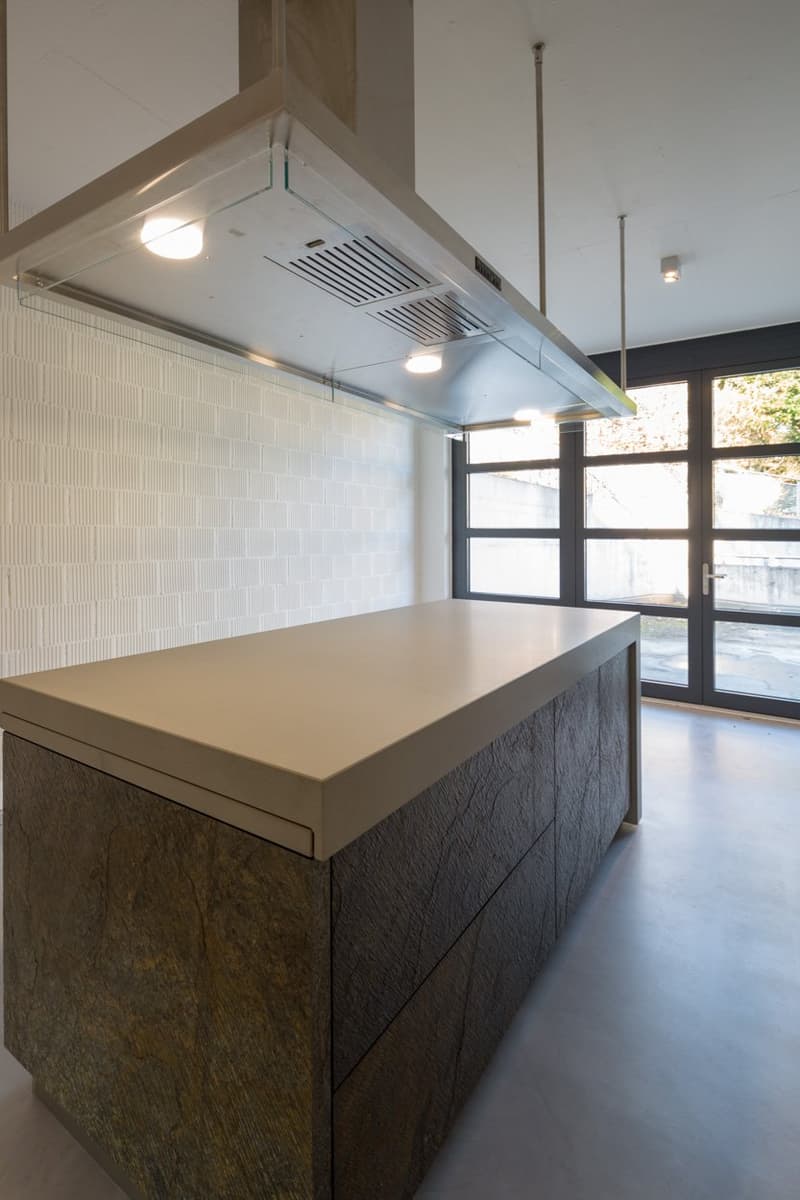 modern kitchen island with a large countertop, wooden cabinets, white tiled wall, glass doors, and ceiling lights