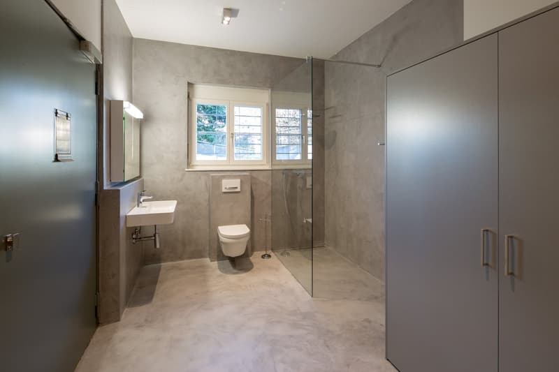 Bathroom with glass shower, white toilet, white sink, gray walls, window