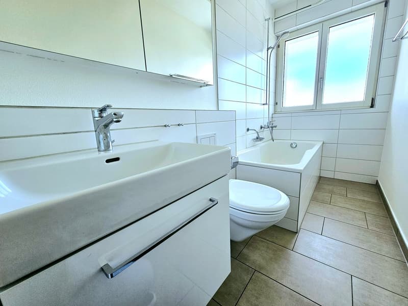 modern bathroom with white tiles, white sink, white bathtub, white toilet, white cabinets, silver faucet