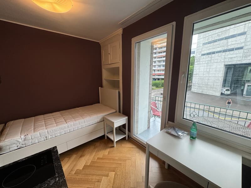 small bedroom with bed, desk, and window with balcony view