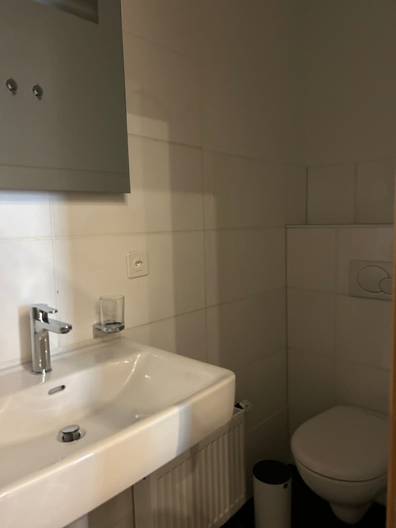 Bathroom with white tiles, white sink, silver faucet, glass cup, white toilet, white trash bin, white radiator