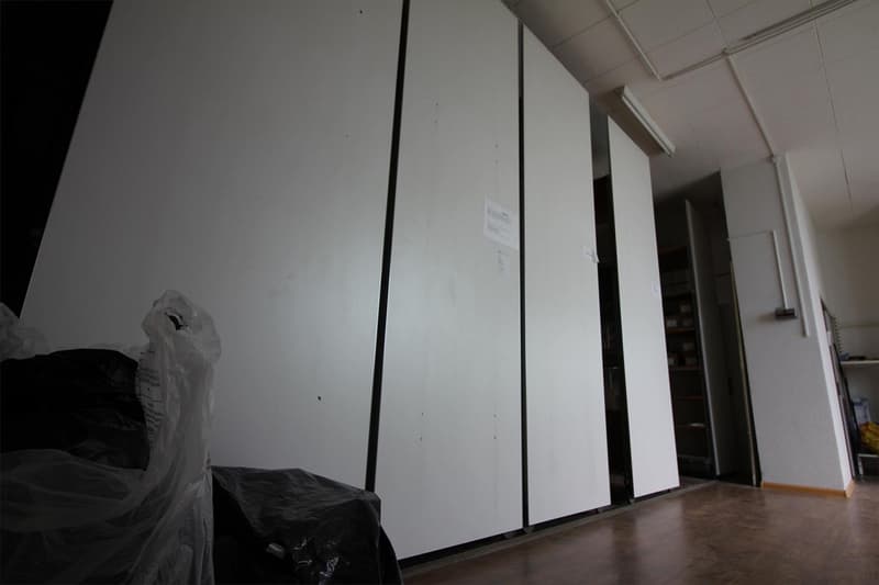 white paneled walls, white ceiling tiles, plastic bags in corner, open sliding door to another room