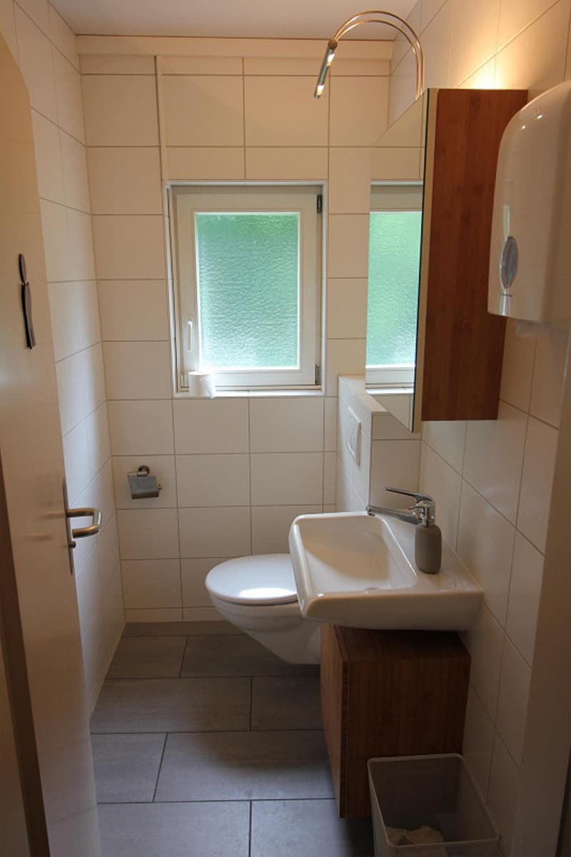 white tiles, window, toilet, sink, mirror, trash can, soap dispenser
