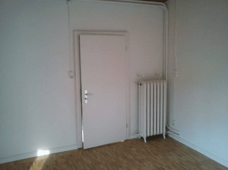 empty room with white walls, wooden floor, radiator, and an open door
