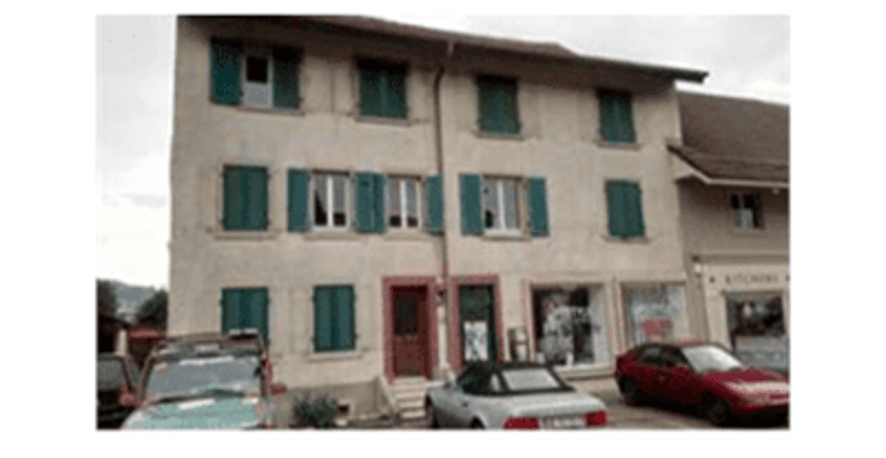 3 story apartment building, white stucco, green shutters, 4 cars parked in front