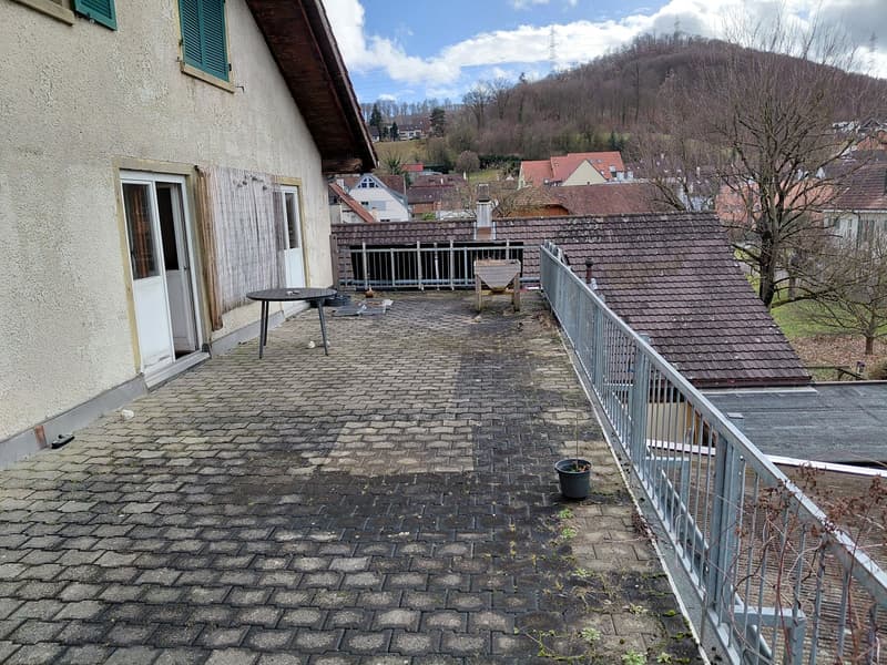 brick paved balcony, metal railings, entrance to a room, table, potted plant, distant houses and hills in view