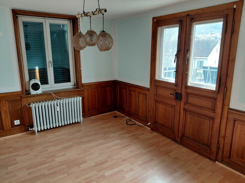 Empty room with wooden paneling, chandelier, radiator, power outlet, two large windows, doors