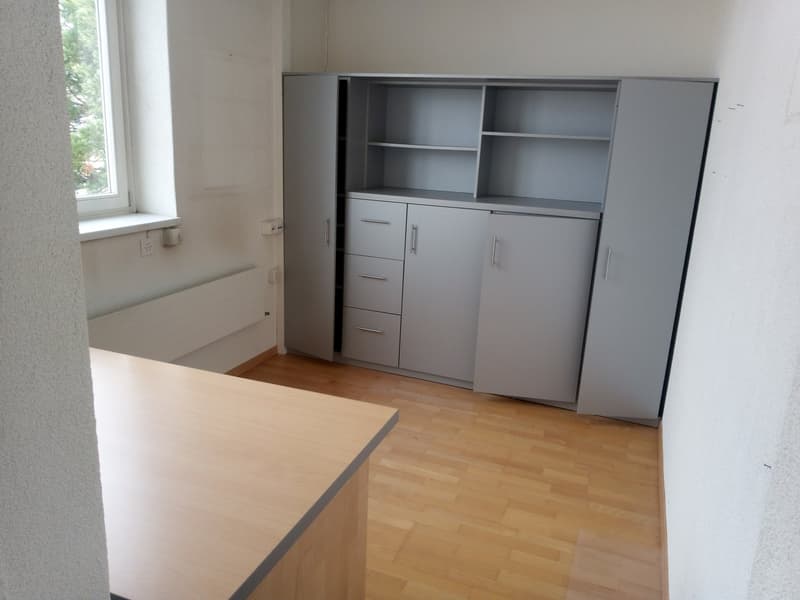 empty room with wooden floor, white walls, large gray cabinets, window, power outlets, and a desk