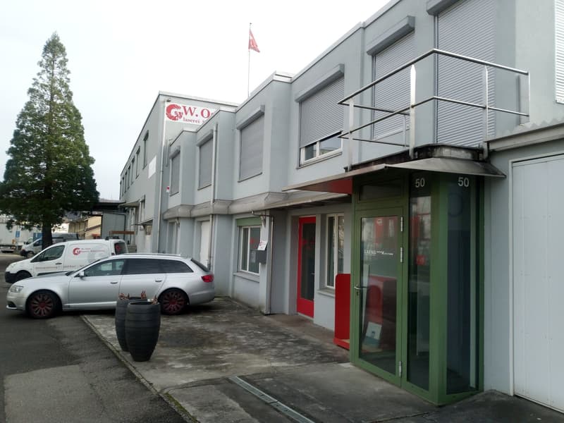 Commercial building with multiple windows, red door, green door, balcony, cars parked in front