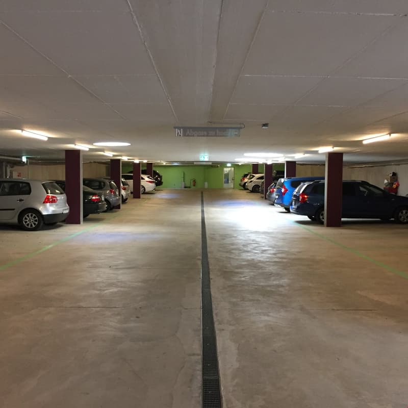 Underground car park with several rows of parking spaces, pillars, and lighting.