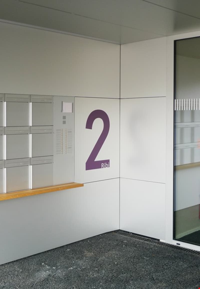 empty room, white walls, gray flooring, mailboxes on the left wall, number 2 on the right wall