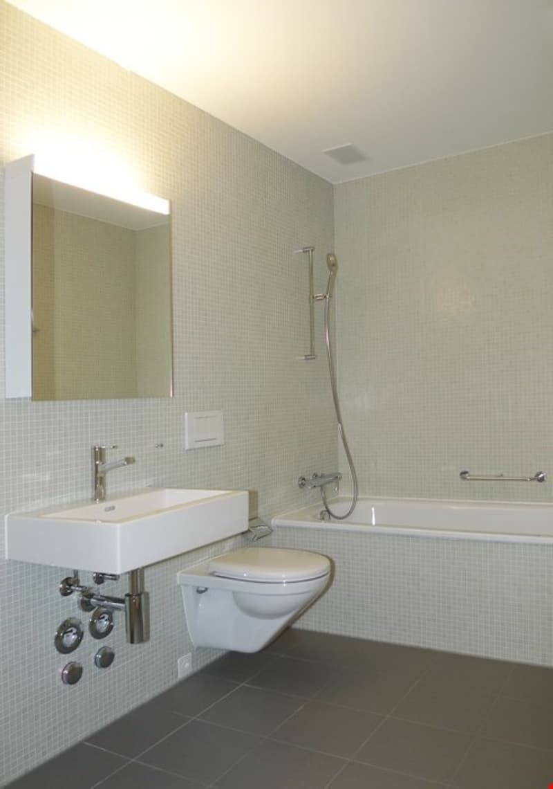 tiled walls, white sink, mirror above sink, modern shower head, bathtub, toilet, power outlet on wall