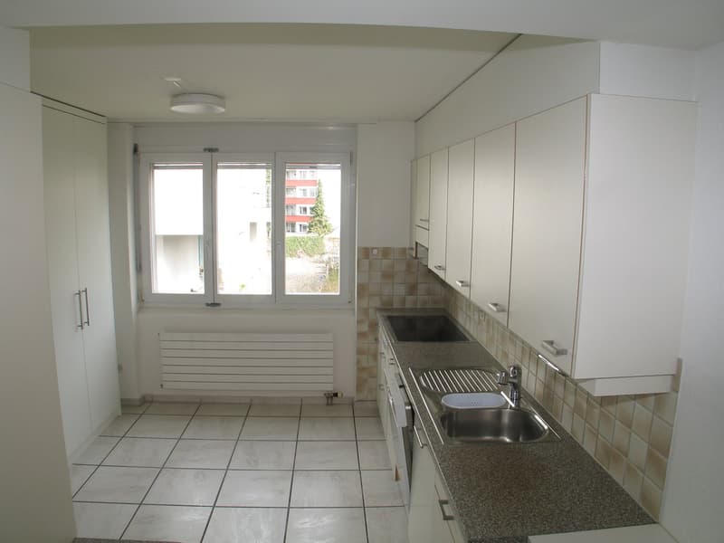 empty kitchen with tiled floor, white cupboards, large windows, underfloor heating, double stainless steel sink, granite counter