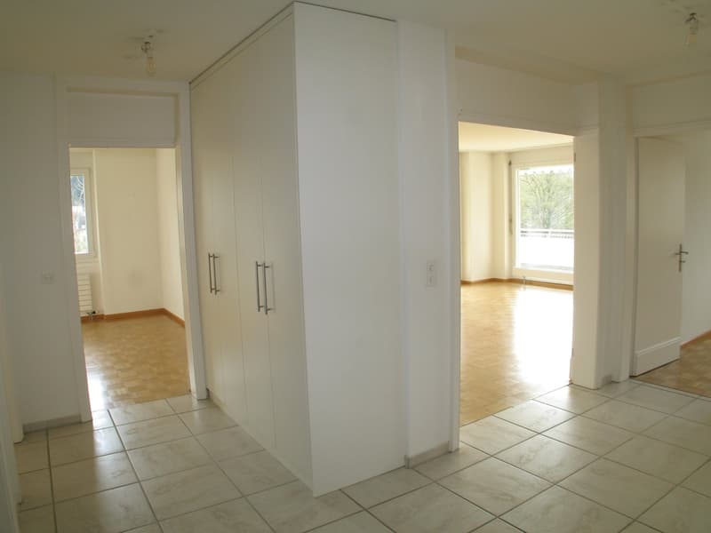 Large room, large white wardrobe, tiled floor, white walls, view of another room with window