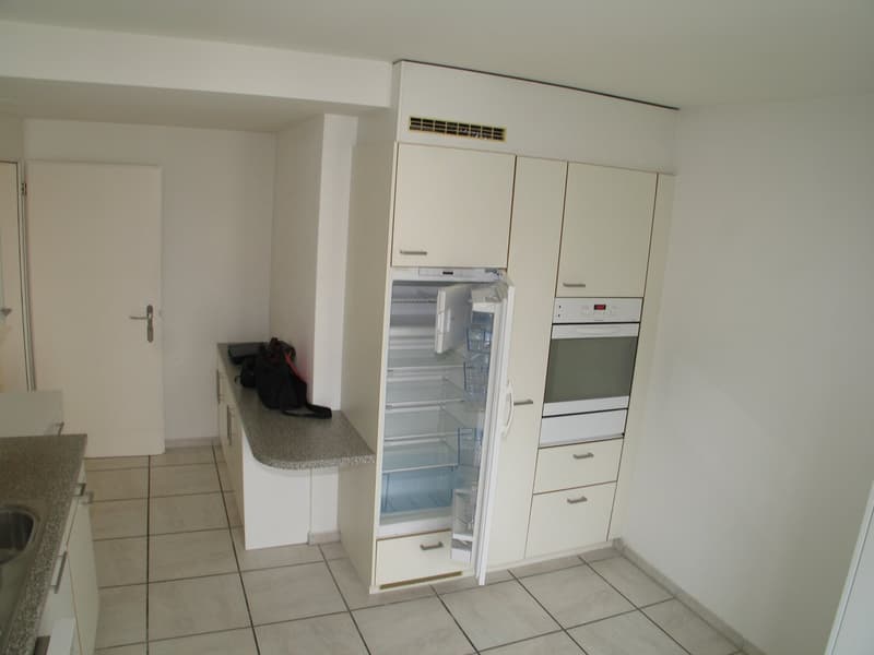 A kitchen with an open refrigerator, oven, cabinets, countertop, and sink