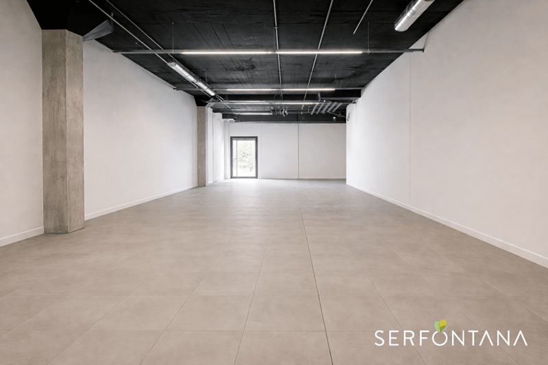 Empty room with tiled floor, white walls, ceiling with metal beams, a central pillar, and a window at the end.