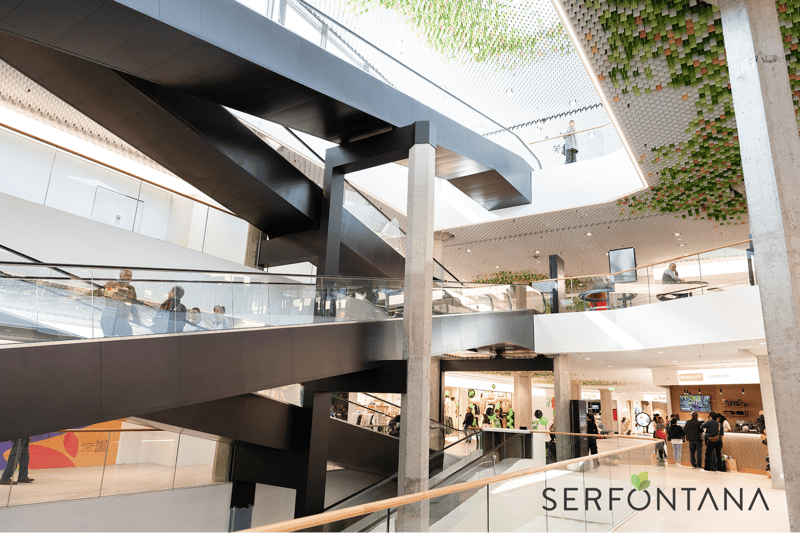 modern building, glass walls, escalators, multiple levels, shops, people walking