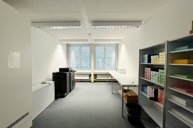 Empty room with desk, printer, storage boxes, white walls, carpet floor, windows with shutters