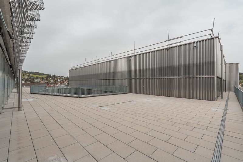 Large industrial-style building with a corrugated metal exterior, surrounded by a paved plaza with a tiled floor.