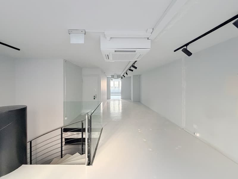 Corridor with white walls, glass railing, spiral staircase, lights on the ceiling, glass door.