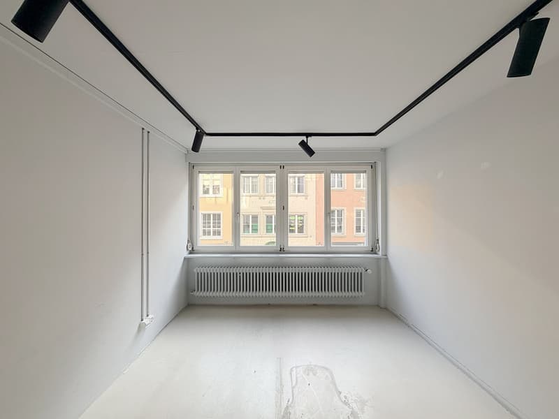 Empty room, white walls, large window with city view, radiator, track lighting