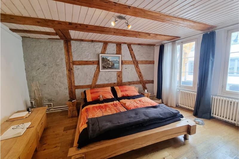 a bedroom with wooden bed, wooden ceiling, wooden side table, two pillows, and two radiators