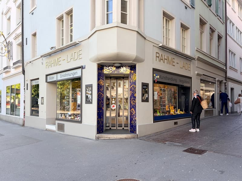 Facade of a building with glass windows and doors, name Rahme-Lade, people walking on the sidewalk