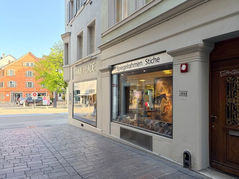 Facade of a building with a shop window, wooden door, and a sign reading 'Spiegelrahmen Stiche'.