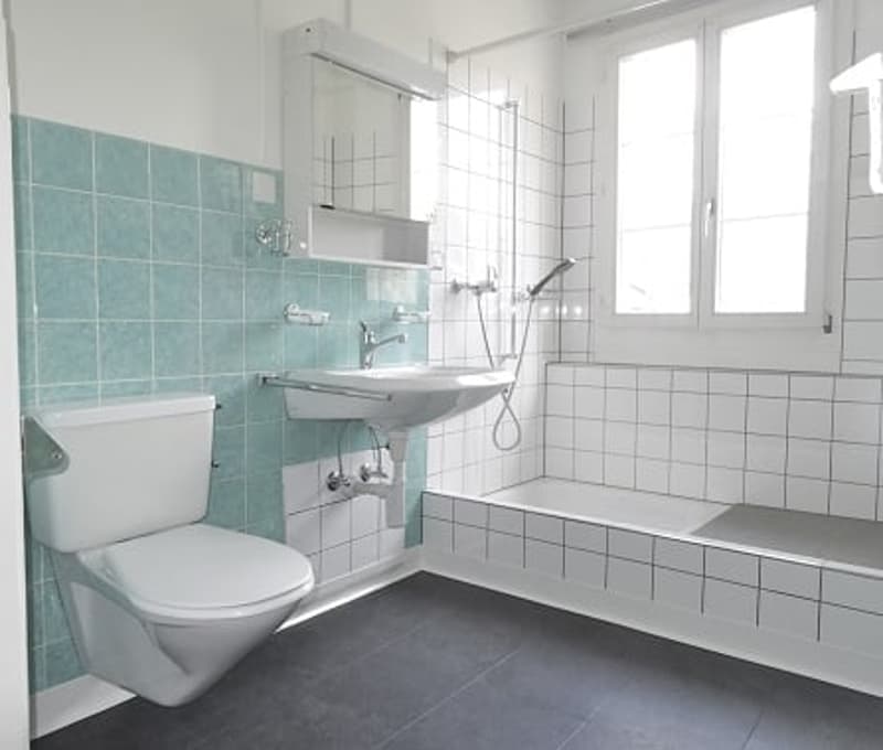 Bathroom with white and turquoise tiles, white toilet, white sink, bathtub, shower head