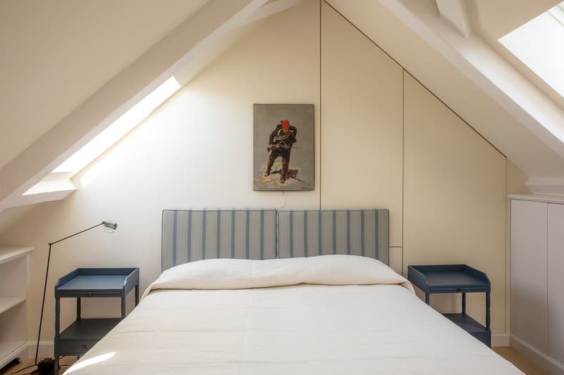 Spacious bedroom with slanted ceiling, large bed with striped headboard, two side tables, and a framed artwork on the wall