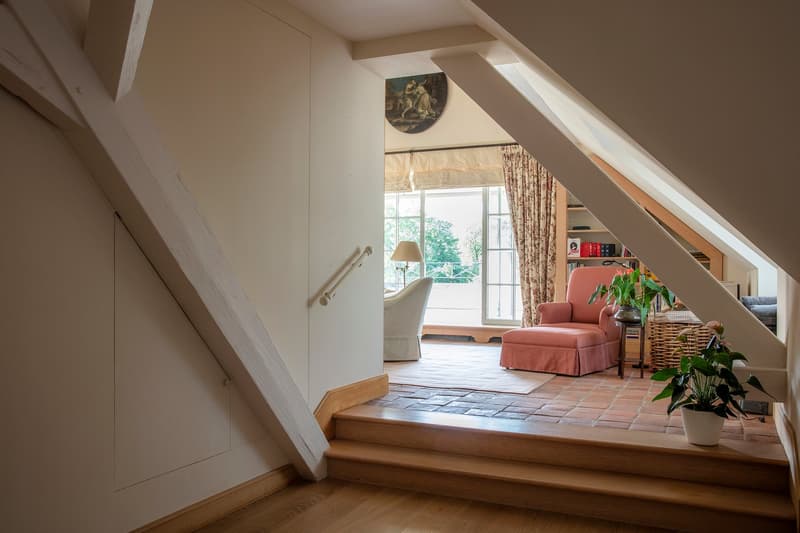 Cozy living room with a raised seating area, large windows overlooking a balcony or terrace, a pink upholstered chair, and a decorative painting on the wall.