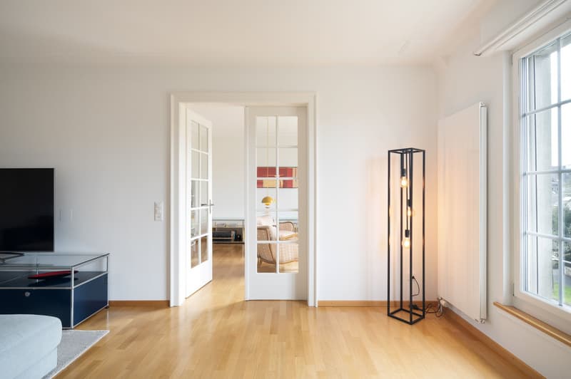 living room with wooden floor, white walls, glass doors, large windows, floor lamp, TV, couch, coffee table