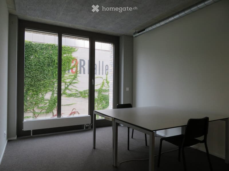 The room is empty, featuring a white desk and two chairs in front of the windows. There is also a white bench under the windows and a radiator is placed on the left side of the window.